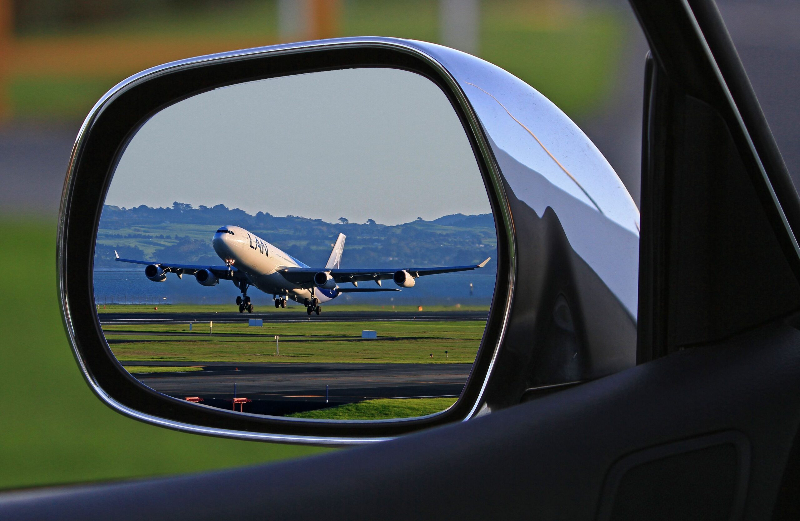 Airport Cab Service in Indore – airport pickup taxi with flight landing reflected in car side mirror for timely transfers